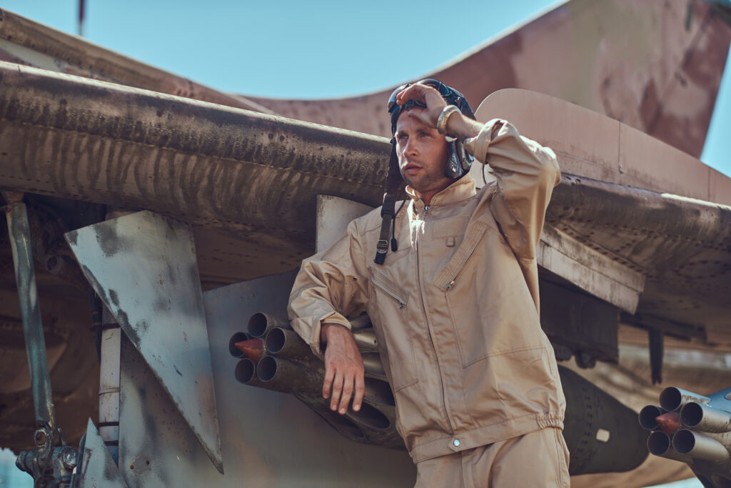 pilot in uniform and flying helmet standing near an old war fighter interceptor in an open air museum.